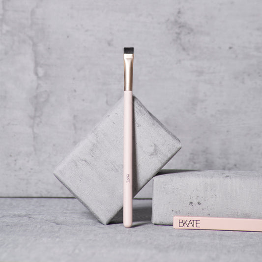 A flat, dense brow concealer and highlighter brush featuring synthetic bristles and a wooden handle, designed for carving out and blending around the eyebrow arch.