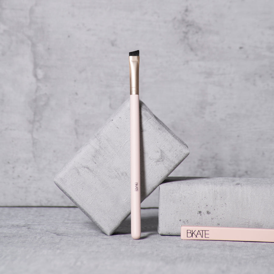 Professional-grade wooden eyebrow brush featuring a slanted synthetic bristle brush head on one end, designed for applying pomades, powders, tints, and henna.