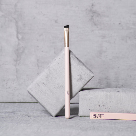Professional-grade wooden eyebrow brush featuring a slanted synthetic bristle brush head on one end, designed for applying pomades, powders, tints, and henna.