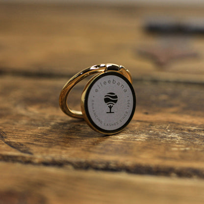 Branded smartphone phone grip and ring holder accessory attached to a phone, designed to secure devices during photography.